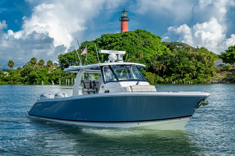 Island Girl II Yacht Photos Pics 2023 Pursuit S 358 Sport boat cruising near a lush island with a lighthouse.