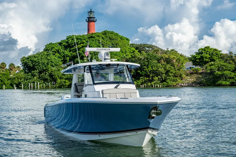 Island Girl II Yacht Photos Pics 2023 Pursuit S 358 Sport boat cruising near a lush island with a lighthouse.