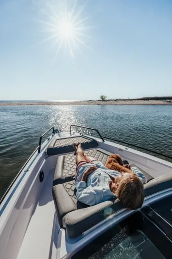  Yacht Photos Pics Person relaxing on Axopar 37XC boat under sunny sky, near a serene shoreline.