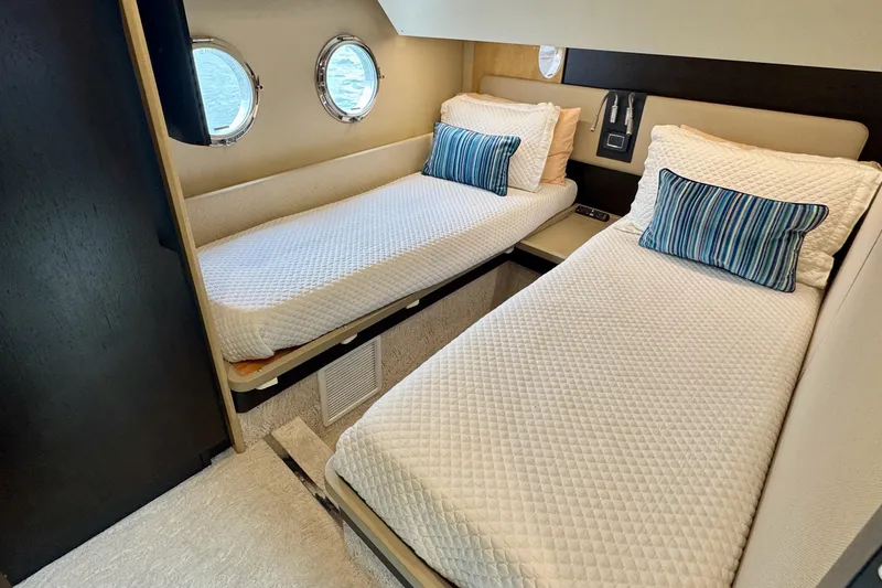 Kiki Yacht Photos Pics Twin beds in a 2016 Azimut 66 yacht cabin with porthole windows and striped pillows.