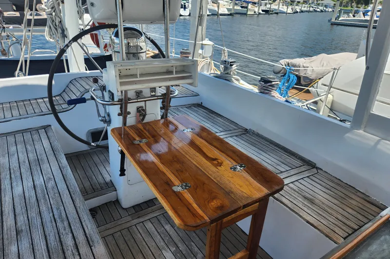Cookie Monster Too Yacht Photos Pics 1982 Tayana Center Cockpit Cutter Ketch with wooden table and steering wheel, docked at marina.