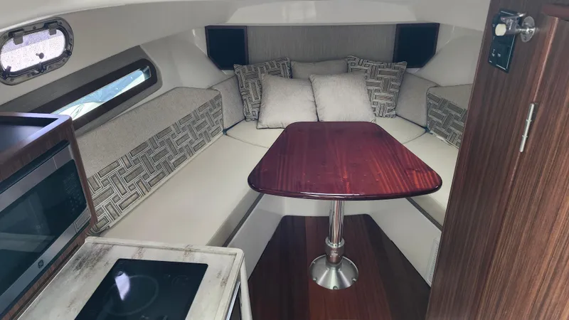  Yacht Photos Pics 2023 Pursuit OS 325 Offshore cabin interior with seating, table, and kitchenette.