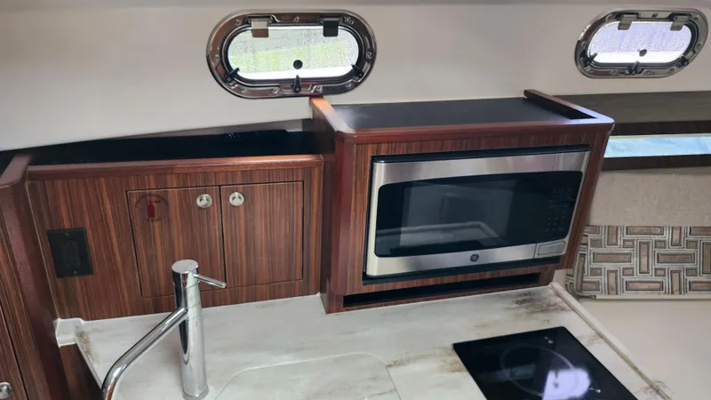  Yacht Photos Pics 2023 Pursuit OS 325 Offshore kitchen with microwave, sink, and wooden cabinetry.