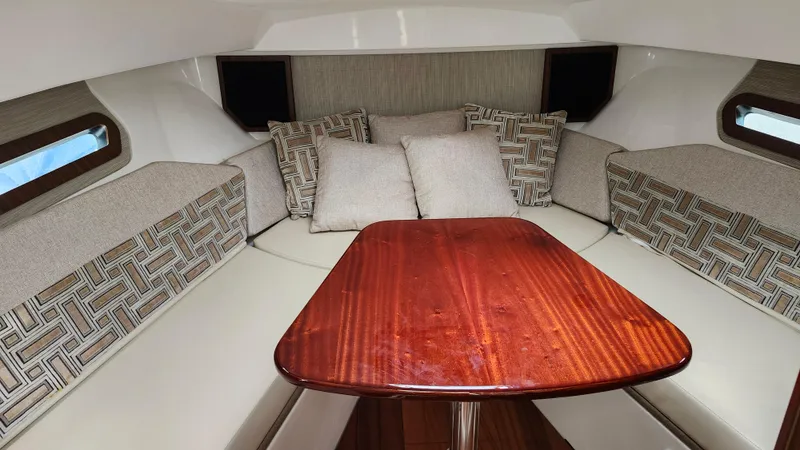  Yacht Photos Pics 2023 Pursuit OS 325 Offshore cabin with cushioned seating and wooden table.