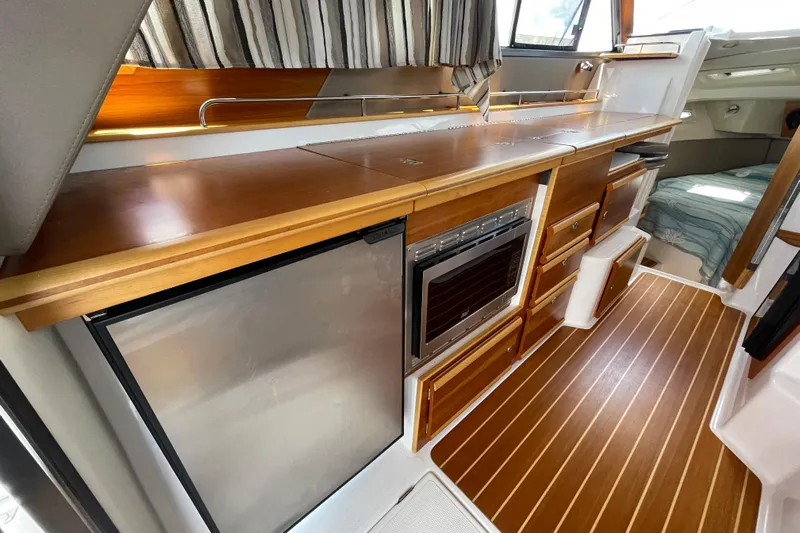 Motivated Yacht Photos Pics 2022 Cutwater C-32 CB interior with wood cabinetry, compact kitchen, and striped curtains.