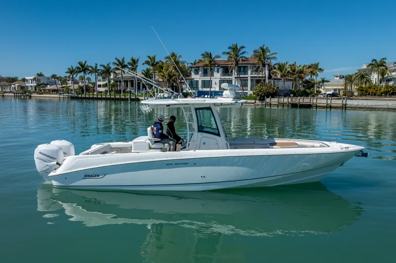 High Voltage Yacht Photos Pics 2013 Boston Whaler 320 Outrage boat on calm water, with palm trees and luxury homes in background.
