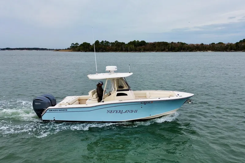 Neverland II Yacht Photos Pics 2022 Grady-White Canyon 271 boat cruising on calm waters near a forested shoreline.