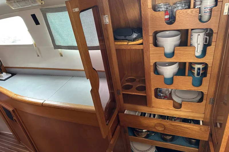 Makani Yacht Photos Pics Interior of 2008 Seawind 1000 XL showing organized wooden kitchen storage with dishes and cups.
