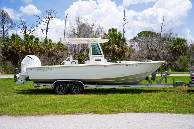  Yacht Photos Pics 2021 Everglades 273 Center Console boat on trailer, parked on grass with trees in background.