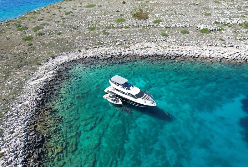  Yacht Photos Pics Aerial view of 2017 Sunseeker Manhattan 66 yacht in clear turquoise waters near rocky shoreline.