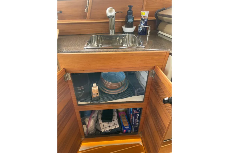 Poseidon&rsquo;s Lanai Yacht Photos Pics 2021 Ranger Tugs R-29 CB kitchen sink with open cabinet displaying dishes and supplies.