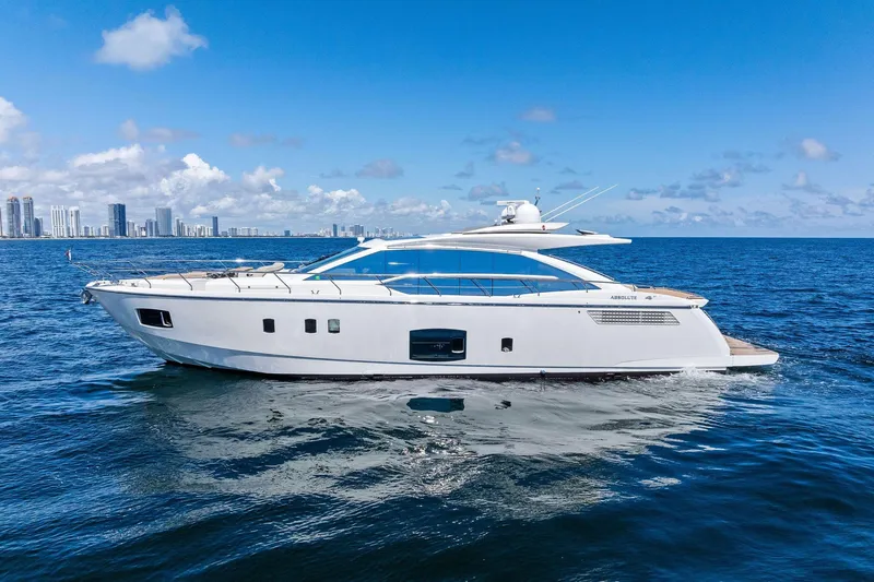 Blue Daksa Yacht Photos Pics Luxury Absolute 64 yacht cruising on open sea, city skyline in background, clear blue sky.