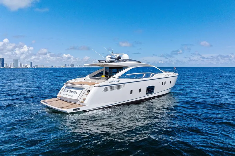 Blue Daksa Yacht Photos Pics Luxury 2013 Absolute 64 yacht cruising on open sea with city skyline backdrop.