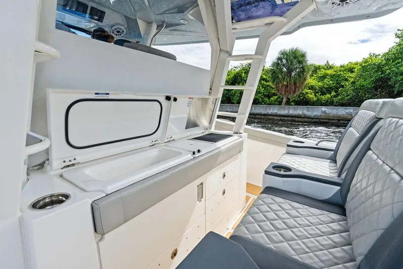 No Vacancy Yacht Photos Pics 2022 Pursuit S 428 Sport boat interior with seating and kitchenette, near lush greenery.