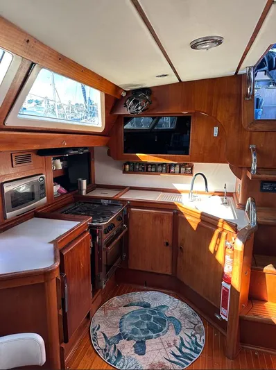 Sarama Yacht Photos Pics 1988 Custom Ancosta Dubois yacht kitchen with wooden cabinetry, stove, sink, and turtle-themed rug.