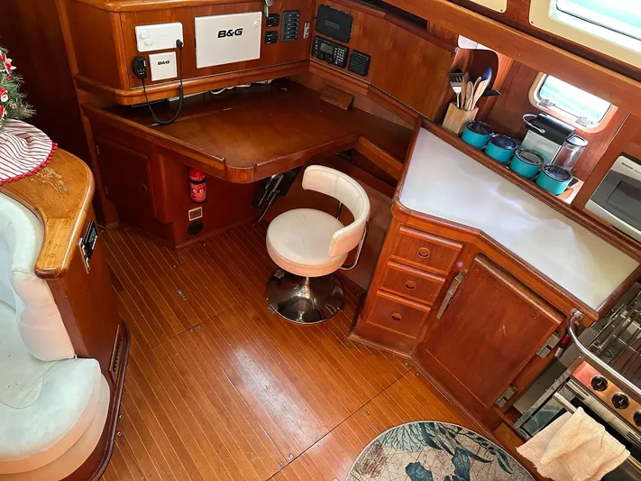 Sarama Yacht Photos Pics Cozy 1988 Ancosta Dubois yacht interior with navigation desk, chair, and compact kitchen area.