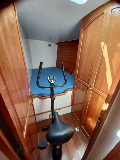 Atanahoue Yacht Photos Pics Compact cabin with exercise bike, wooden cabinets, and blue bedding on a Custom Paladin 60 yacht.