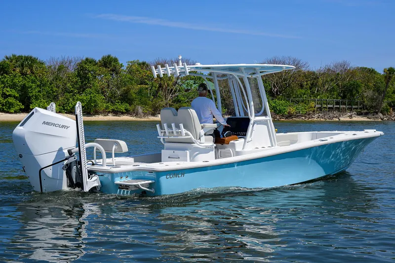  Yacht Photos Pics 2024 Conch 25 boat cruising on water with Mercury engine, clear sky, and lush shoreline.