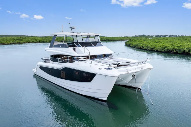  Yacht Photos Pics 2026 Aquila 50 Yacht cruising on a serene river under a clear blue sky.