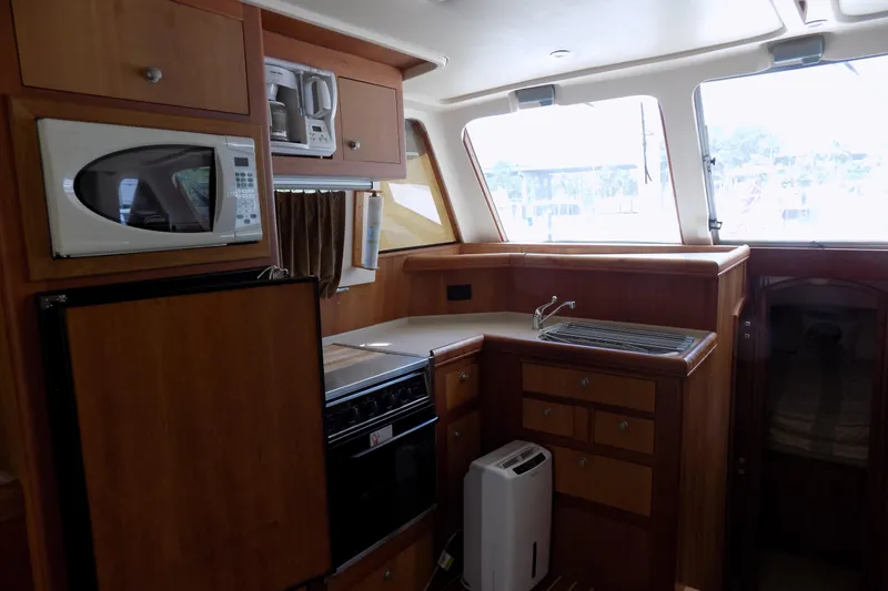  Yacht Photos Pics 2004 Mainship 390 Trawler kitchen with microwave, stove, and wooden cabinetry.