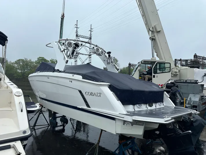  Yacht Photos Pics 2022 Cobalt R8 Surf boat on a lift, covered, with a crane in the background.
