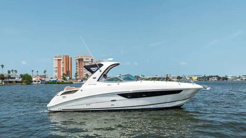  Yacht Photos Pics 2016 Sea Ray 310 Sundancer cruising on a sunny day near waterfront buildings.