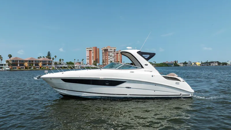  Yacht Photos Pics 2016 Sea Ray 310 Sundancer yacht cruising on a sunny day near waterfront buildings.