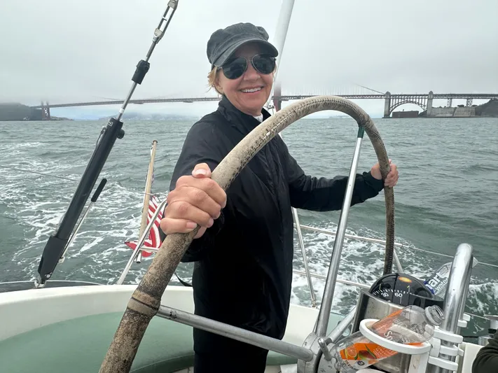 Ayla Yacht Photos Pics Person steering 1991 Beneteau First sailboat near a bridge on a cloudy day.