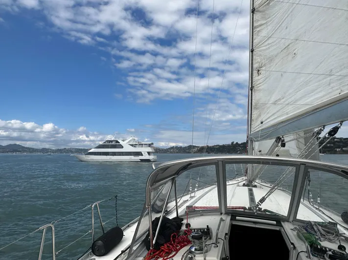 Ayla Yacht Photos Pics Sailing on a 1991 Beneteau First yacht with a ferry in the background, under a blue sky.