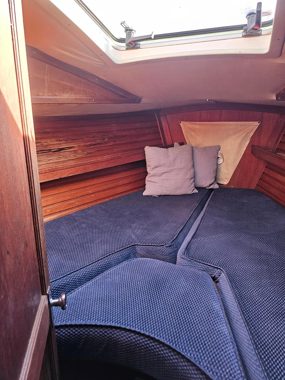 Cozy cabin interior of 1984 Schock NY 36 sailboat with blue cushions and wooden paneling.