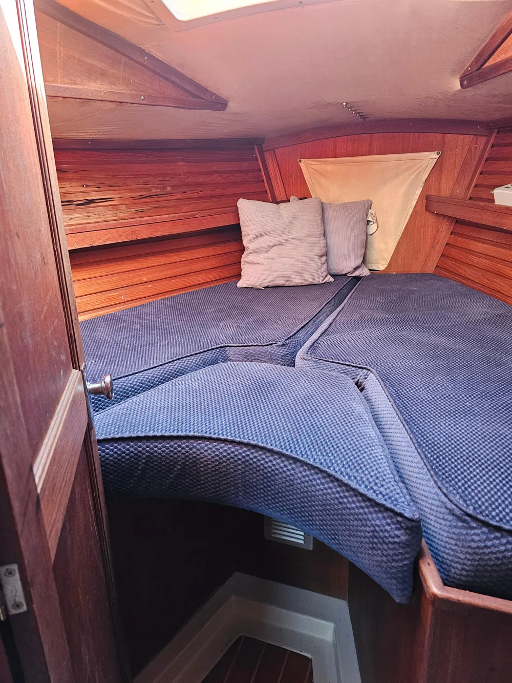 Cozy cabin interior of 1984 Schock NY 36 sailboat with blue bedding and wooden paneling.