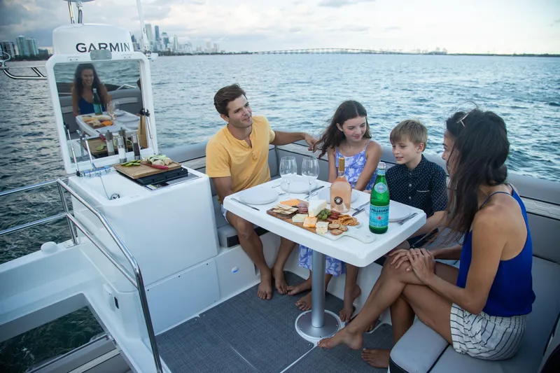  Yacht Photos Pics Family enjoying a meal on a 2024 Jeanneau NC 1295 Fly boat, with city skyline backdrop.
