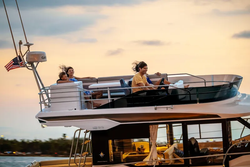  Yacht Photos Pics 2024 Jeanneau NC 1295 Fly yacht cruising at sunset with passengers enjoying the view.