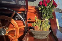 Wooden helm of 1993 Custom Gulet Motorsailer with cacti and roses in sunlight.