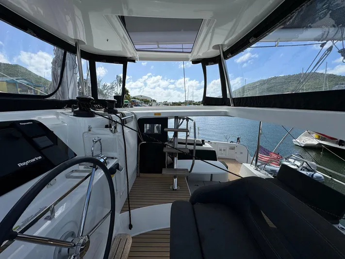 Bluevana Yacht Photos Pics 2023 Lagoon 42 yacht cockpit with steering wheel, seating, and scenic marina view.