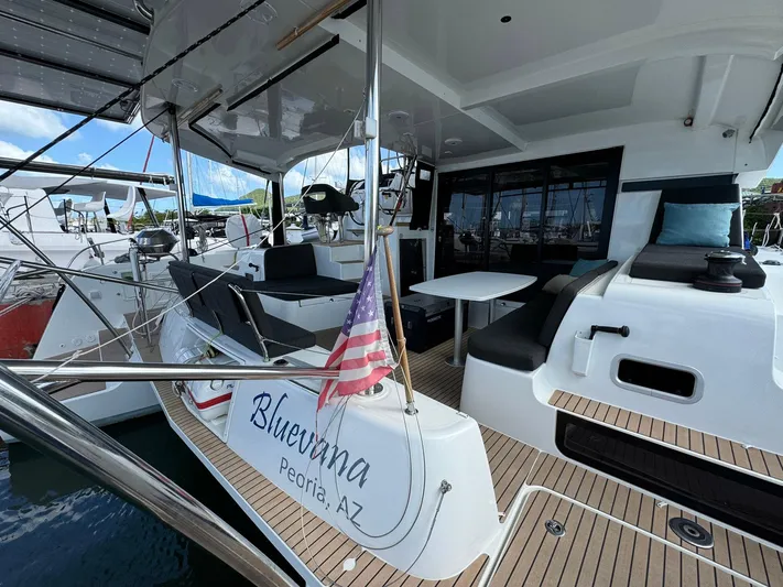 Bluevana Yacht Photos Pics 2023 Lagoon 42 catamaran with American flag, docked, featuring spacious deck and seating area.