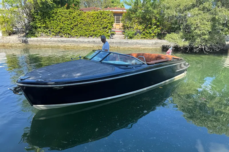  Yacht Photos Pics 2018 Chris-Craft Capri 27 boat on calm water, surrounded by lush greenery.
