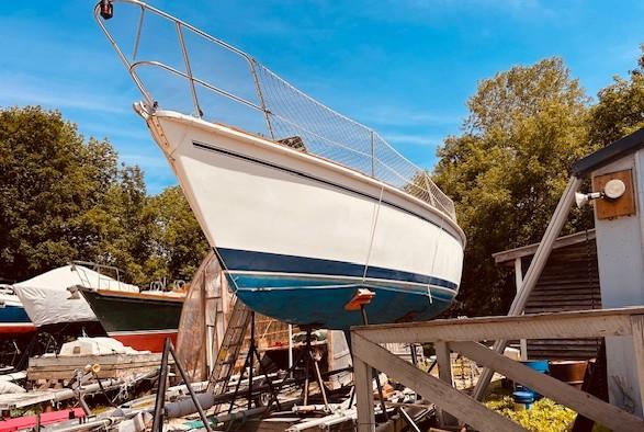 1986 Pearson 28 sailboat on dry dock, surrounded by trees and blue sky.