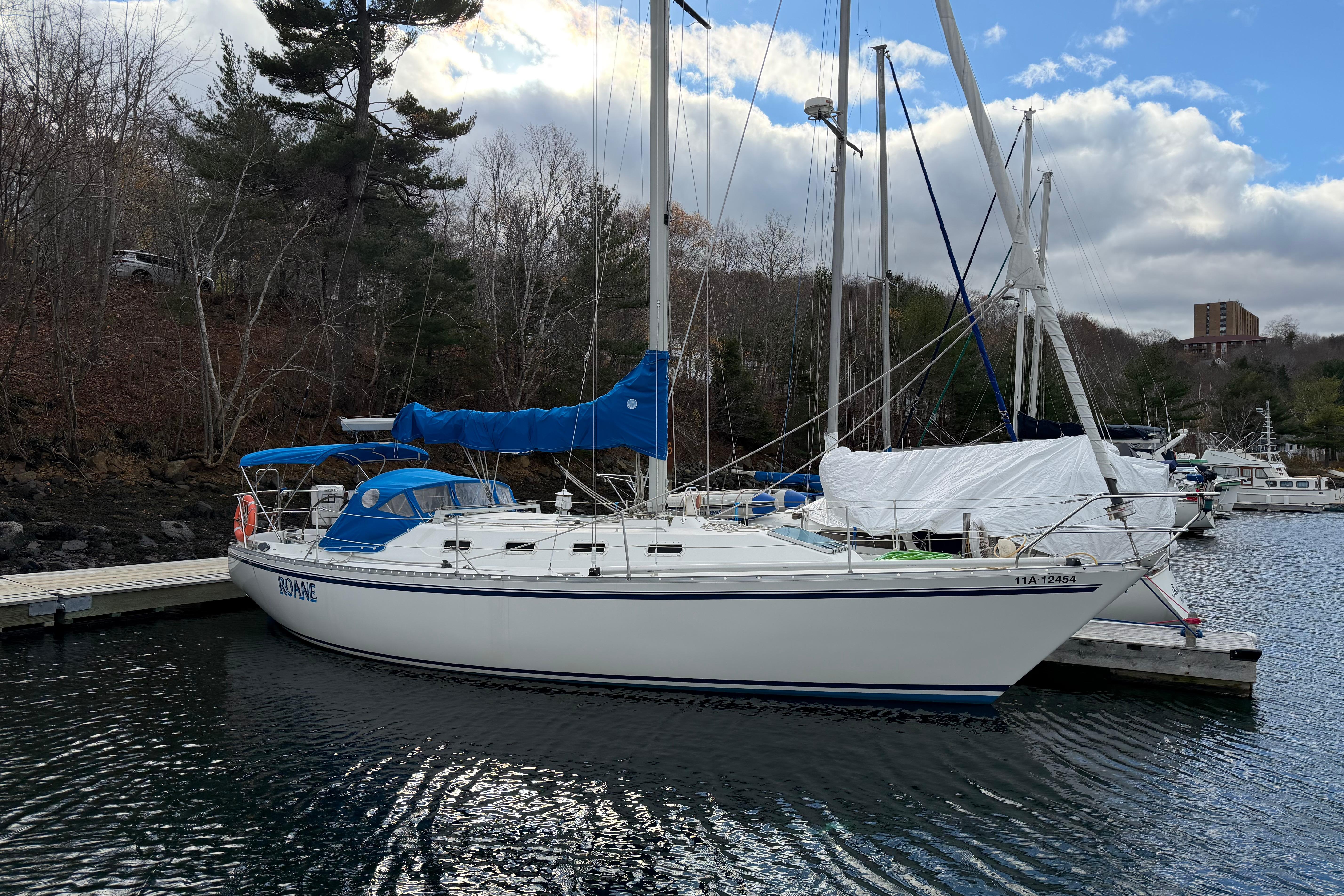 1985 CS 36 sailboat docked at a marina with blue sky and trees.