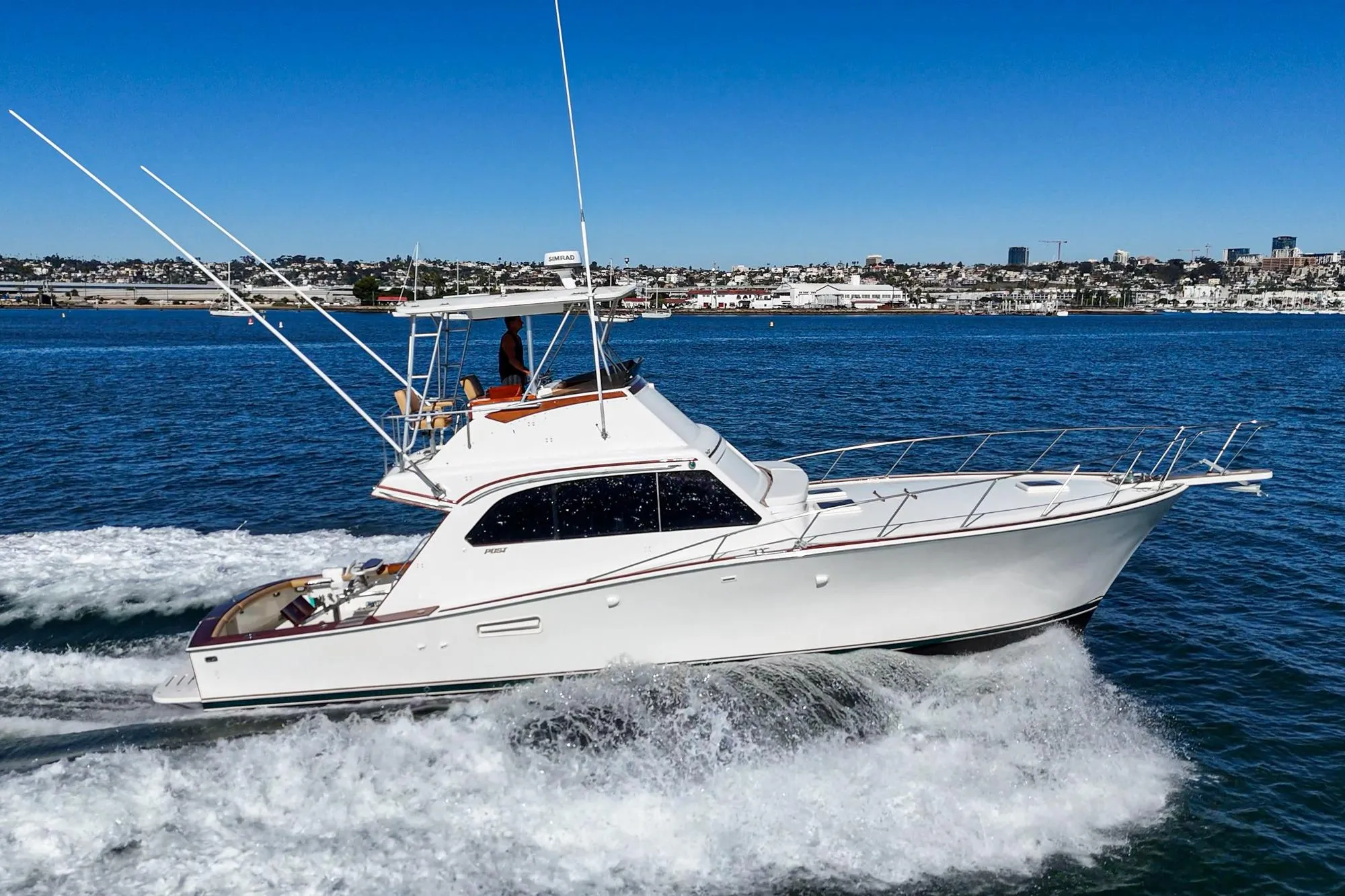 1984 Post 43 yacht cruising on blue water with cityscape background.