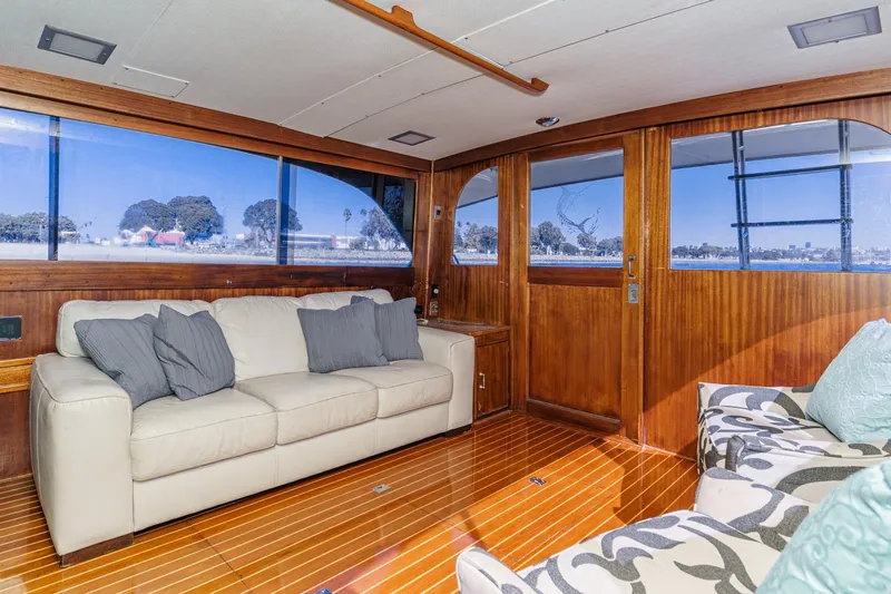 Un Dia Yacht Photos Pics Luxurious yacht interior with wooden paneling, cream sofa, and large windows offering scenic views.