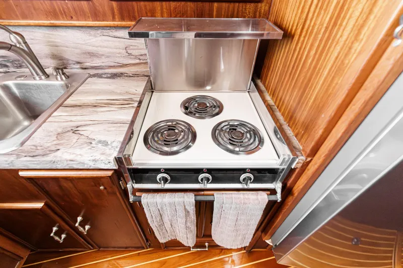 Un Dia Yacht Photos Pics Compact kitchen with electric stove, marble countertop, and wooden cabinetry in a 1984 Post 43 model.