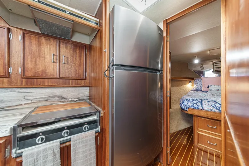 Un Dia Yacht Photos Pics Compact boat kitchen with stainless steel fridge, wooden cabinets, and cozy sleeping area.