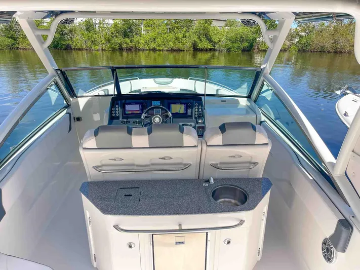  Yacht Photos Pics 2021 Chaparral 300 OSX boat interior with helm, seating, and kitchenette on calm water.