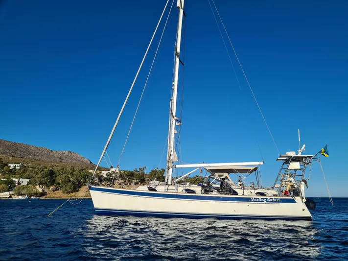 Surfing Safari Yacht Photos Pics 2010 Hallberg-Rassy 40 sailboat anchored in clear blue waters near a rocky coastline.