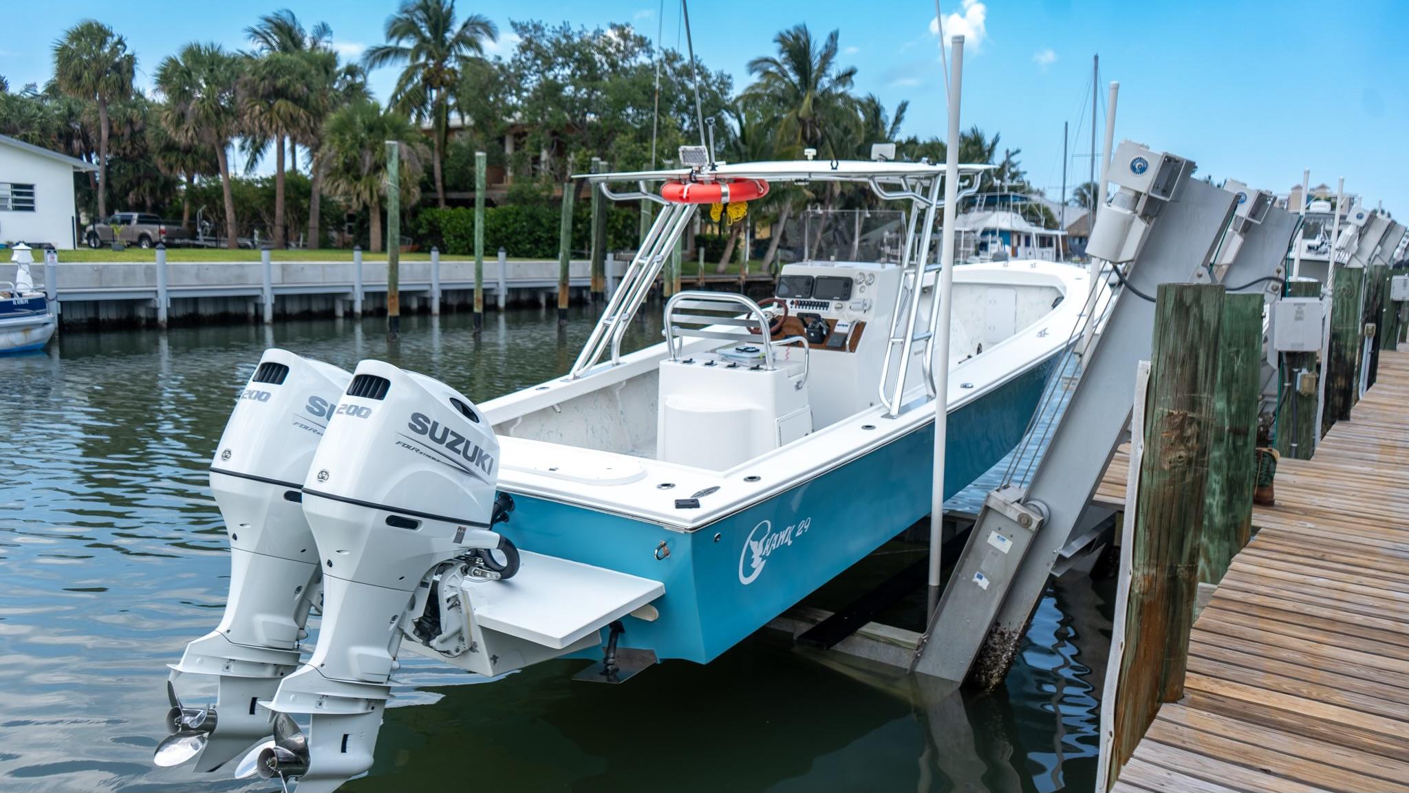 2021 C-Hawk 29CC boat with twin Suzuki engines docked by palm trees.