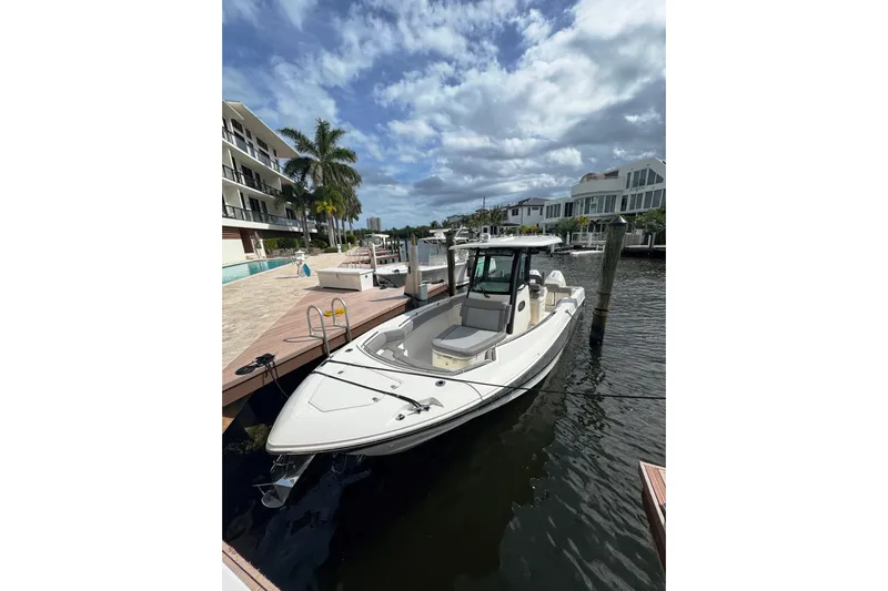  Yacht Photos Pics 2024 Boston Whaler 280 Outrage docked by waterfront homes under a partly cloudy sky.