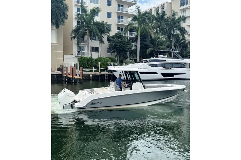  Yacht Photos Pics 2024 Boston Whaler 280 Outrage cruising near waterfront buildings and palm trees.