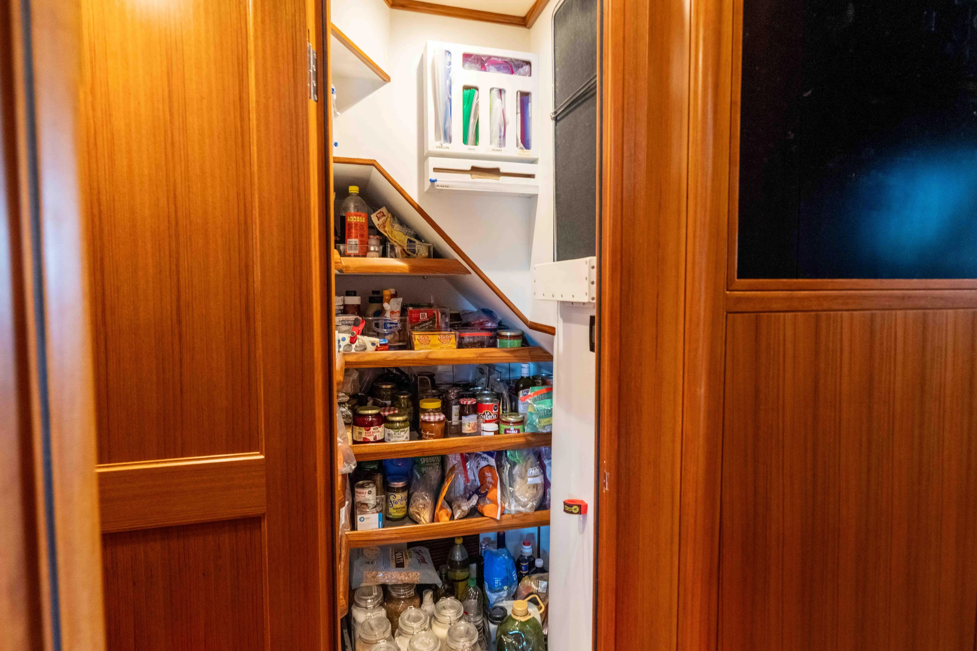 Martini Yacht Photos Pics Pantry storage inside 2022 Nordhavn N63 yacht, featuring wooden shelves and various food items.