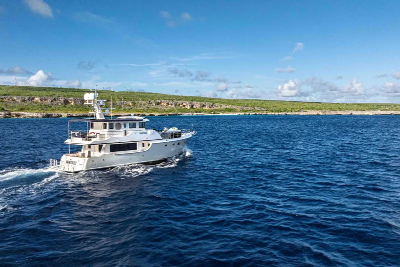 Martini Yacht Photos Pics 2022 Nordhavn N63 yacht cruising on blue ocean near green coastline.